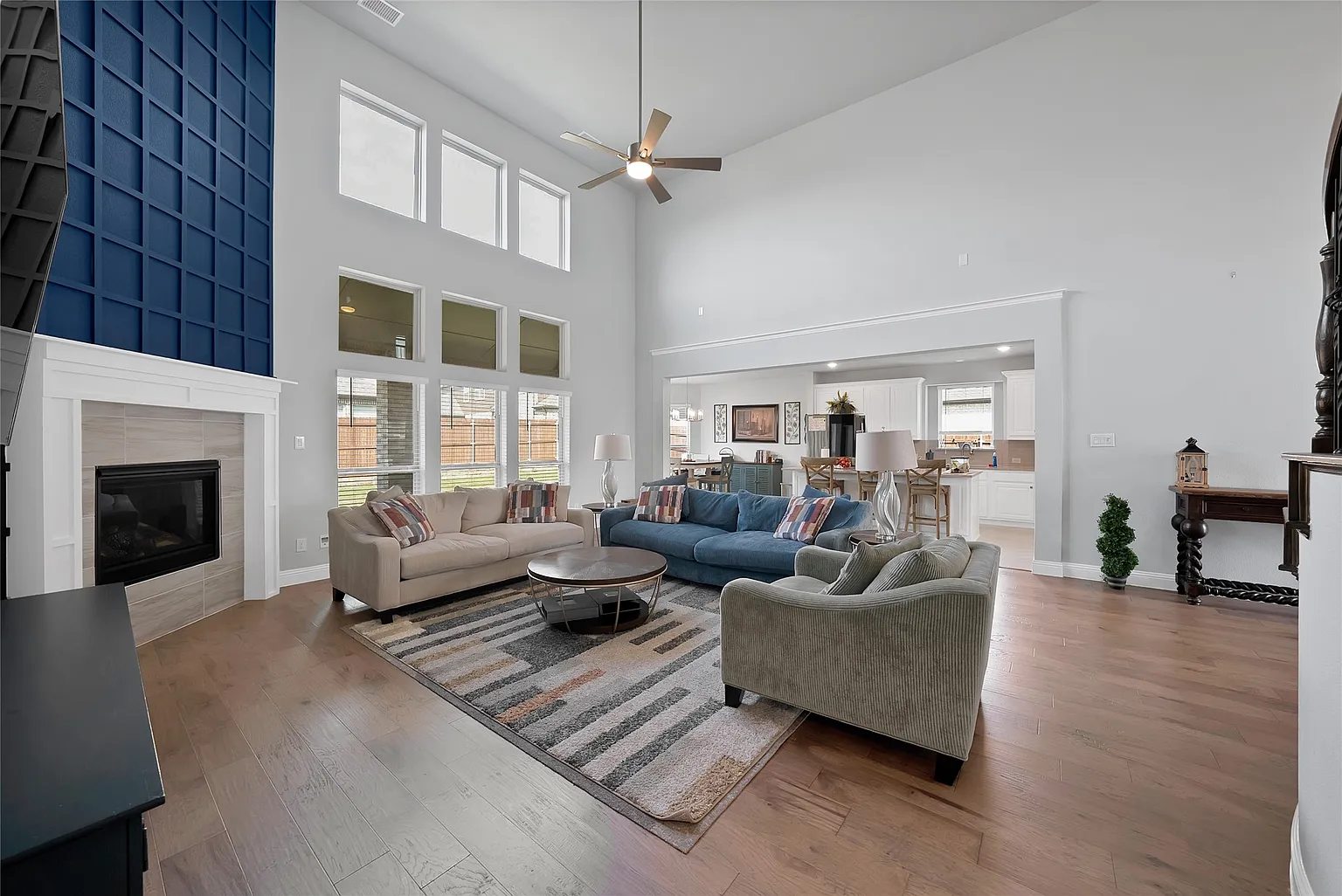 Living room with tall windows, blue accent wall, fireplace and open view to the kitchen.