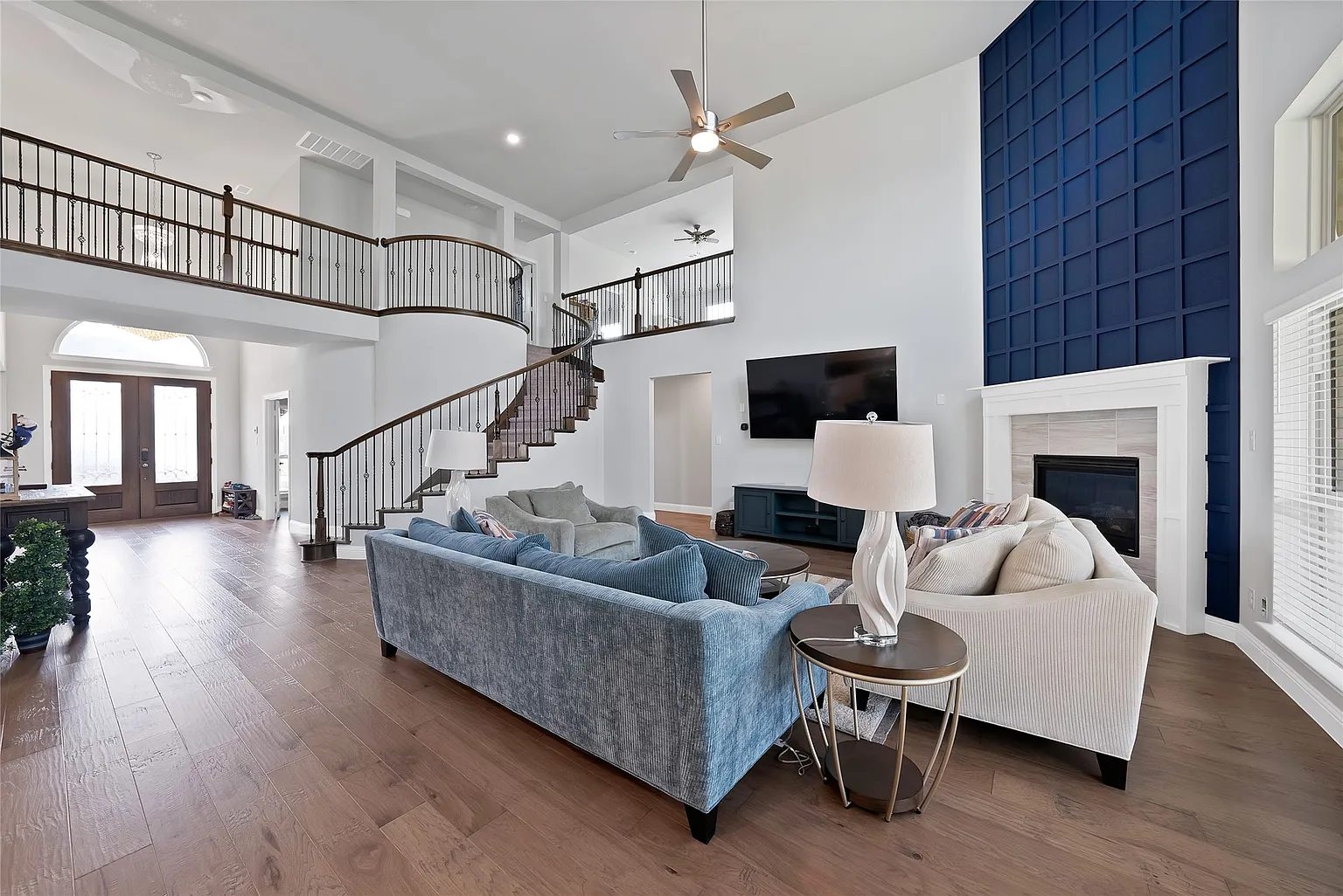 Two-story living room, curved staircase, fireplace and blue architectural accent wall.