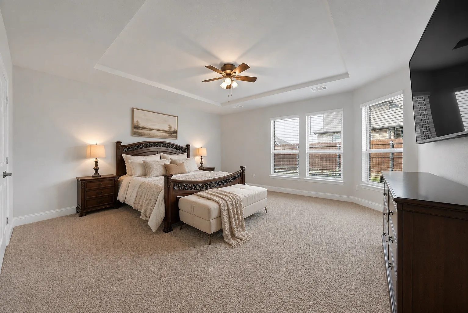 Primary bedroom with a tray ceiling, windows and carpet.