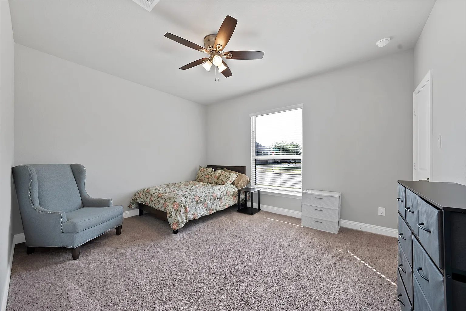A carpeted bedroom with a single bed, chair and ceiling fan.